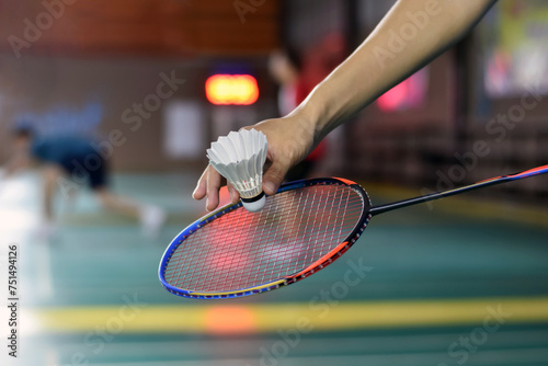 Badminton player holds racket and white cream shuttlecock in front of the net before serving it to another side of the court, soft focus. © Sophon_Nawit