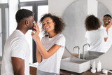 Young black couple shares flirty moment moisturizing skin in bathroom