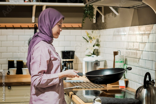Young asian woman in hijab cooking in the kitchen photo