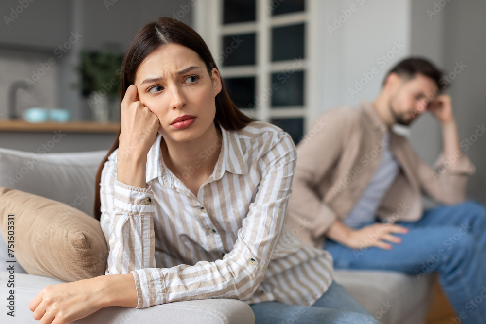 Upset young couple with problems sitting apart on sofa Upset young couple with problems sitting apart on sofa