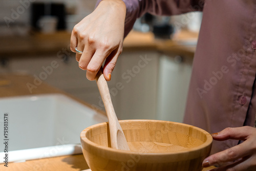 a woman's hand holding a wooden spatula making dough with a wooden bowl, close-up shot in the kitchen photo