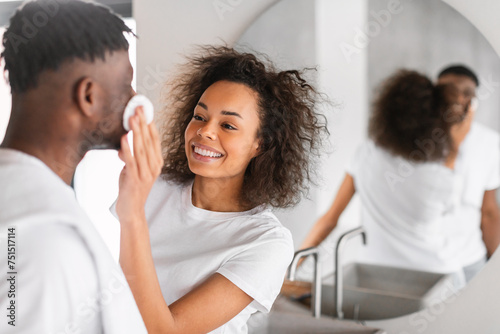 African wife applies skincare products to husband's face at bathroom