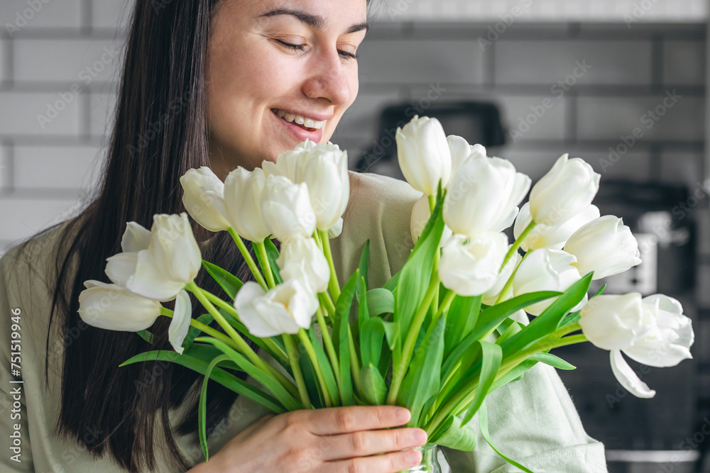 A woman holds a vase with white tulips in a kitchen interior. A woman holds a vase with white tulips in a kitchen interior.