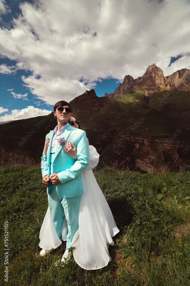 A young man and his wife stand in an embrace high in the mountains against the backdrop of epic rocks on a sunny day. Newlyweds wedding couple in the mountains A young man and his wife stand in an embrace high in the mountains against the backdrop of epic rocks on a sunny day. Newlyweds wedding couple in the mountains