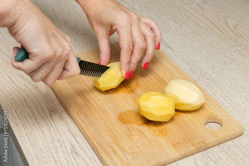 housewife cuts potatoes in half on a kitchen board
