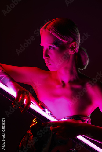 attractive peculiar woman in metallic futuristic attire holding pink LED lamp stick and looking away