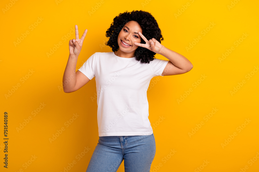 Portrait of good mood gorgeous girl with curly hairstyle wear white t-shirt showing v-sign on eye isolated on yellow color background Portrait of good mood gorgeous girl with curly hairstyle wear white t-shirt showing v-sign on eye isolated on yellow color background
