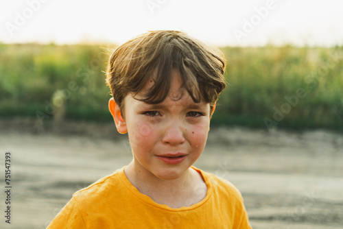 Portrait of a boy in nature. A boy in an orange T-shirt is crying in nature. Non-positive child, lifestyle. photo