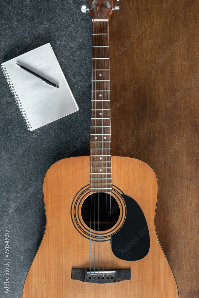 Acoustic guitar and notebook on a textured black and wooden background.
