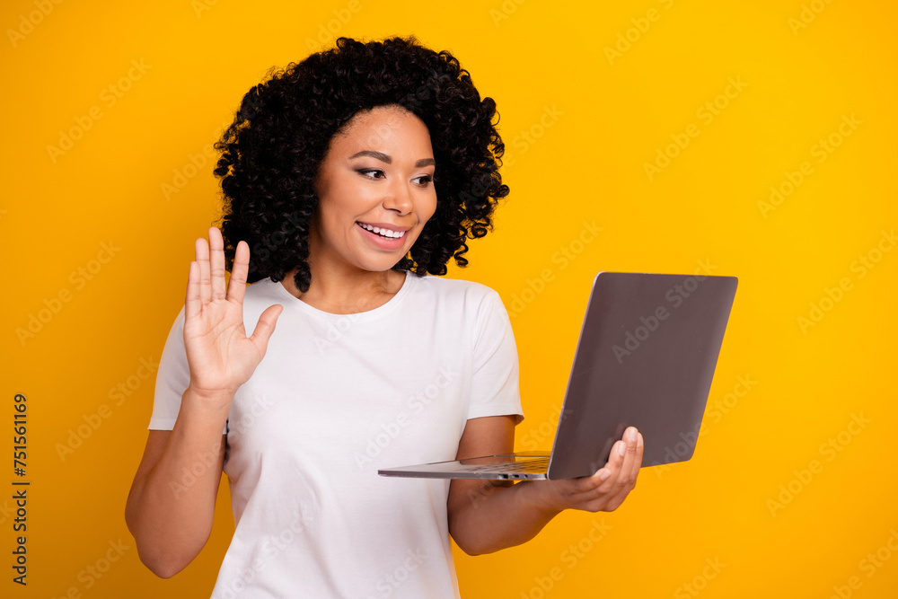 Portrait of charming girl with curly hairstyle wear white t-shirt waving palm on laptop webcam say hi isolated on yellow color background Portrait of charming girl with curly hairstyle wear white t-shirt waving palm on laptop webcam say hi isolated on yellow color background