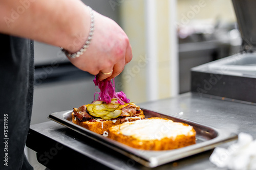 A chef assembles a gourmet sandwich with fresh vegetables and grilled meat on toasted bread in a professional kitchen