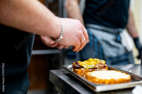 A chef assembles a gourmet sandwich with fresh vegetables and grilled meat on toasted bread in a professional kitchen