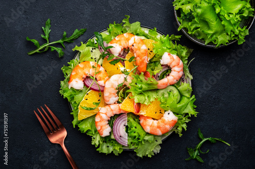 Fresh shrimp salad with orange, lettuce, cucumbers, red onion and sesame seeds with olive oil, black background, top view
