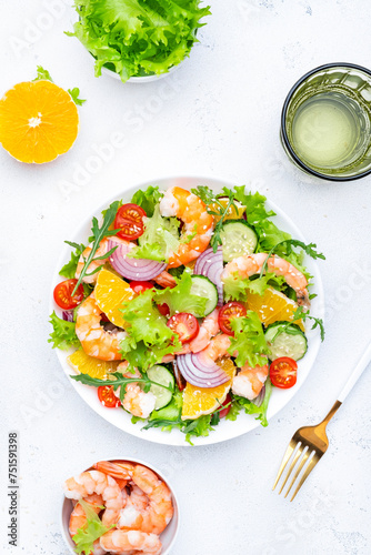 Fresh delicious shrimp salad with orange, lettuce, tomatoes, cucumbers, onions and sesame seeds with olive oil, white background, top view