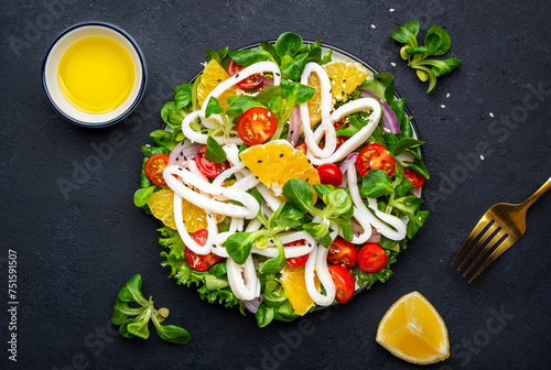 Fresh salad with squid, oranges, cherry tomatoes, lamb lettuce and olive oil with lemon juice dressing, black table background, top view