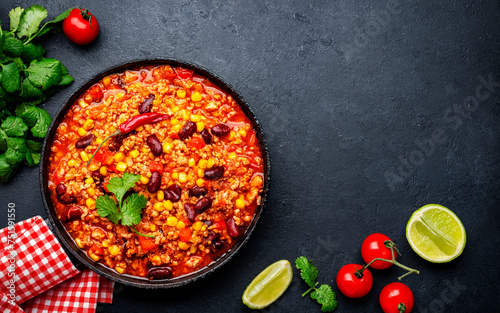 Chili con carne, mexican dish with minced beef, red beans, paprika, corn, cilantro and red peppers in spicy tomato sauce, tex-mex cuisine, black table background, top view