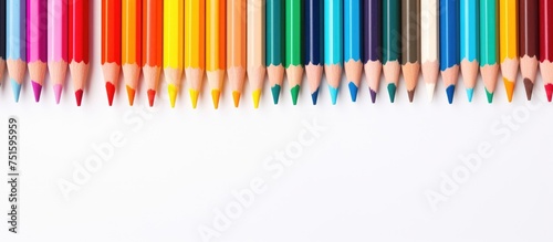 Multiple colorful pencils neatly lined up on a clean white surface, creating a visually appealing pattern. The pencils are arranged in a row, showcasing their vibrant hues and sharp tips, ready for