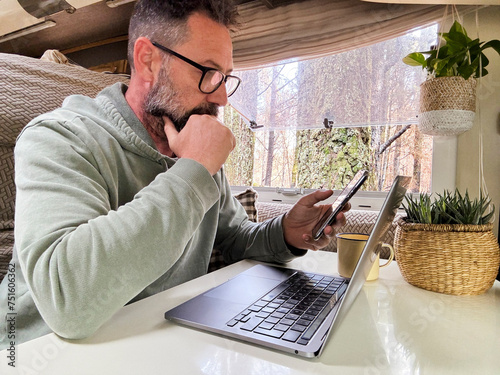 One adult man using a laptop inside a camper van in vanlife remote worker digital nomad lifestyle. Small online business people concept. Mature male with beard and glasses use computer indoor. Nature photo