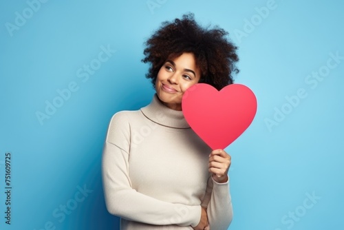 Content woman posing with a red heart cutout, thoughtful expression.