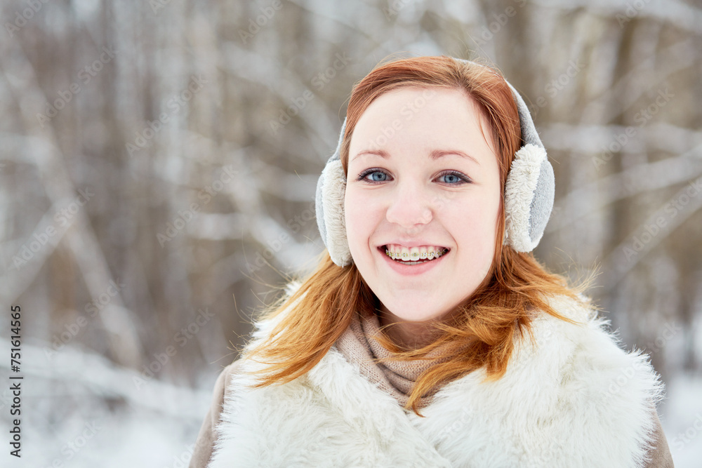 Humeral portrait of red-haired girl with braces on teeth in earmuffs at winter park Humeral portrait of red-haired girl with braces on teeth in earmuffs at winter park