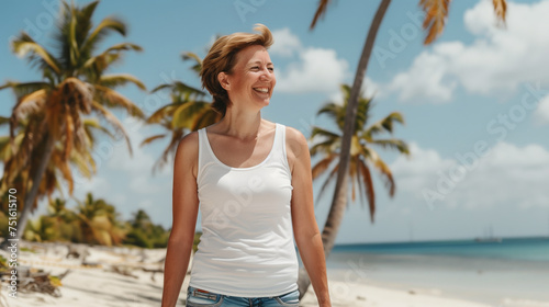 A woman in a white T-shirt walks along the sandy shore of the ocean against a palu backdrop and smiles
