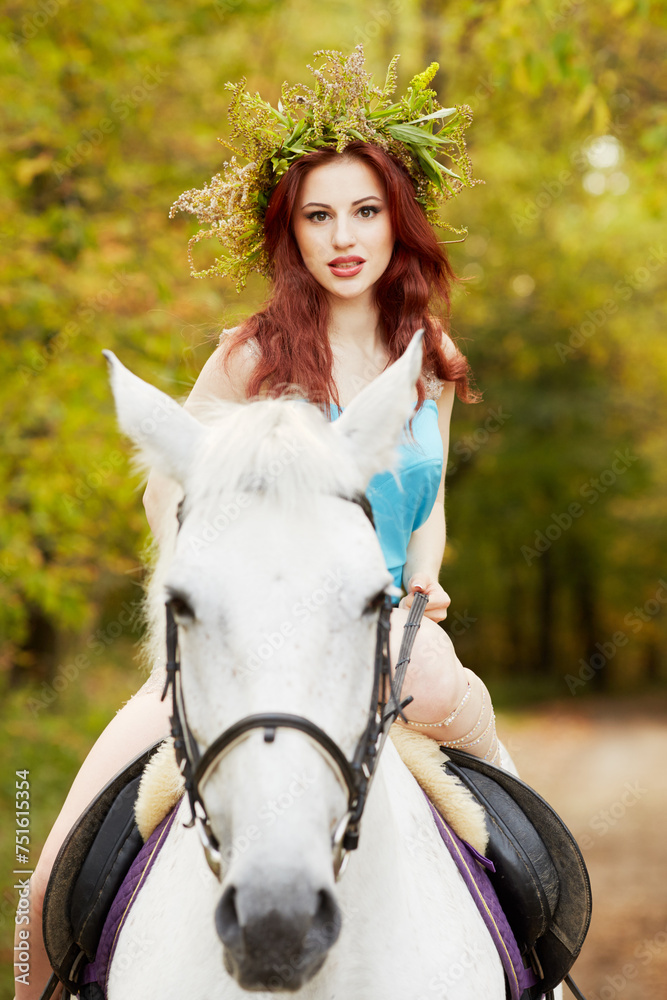 Obraz premium Red-haired woman with floral wreath on head rides on white horse in park