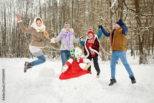 Happy family of four jumps holding hands around stuffed dummy Maslenitsa in winter park