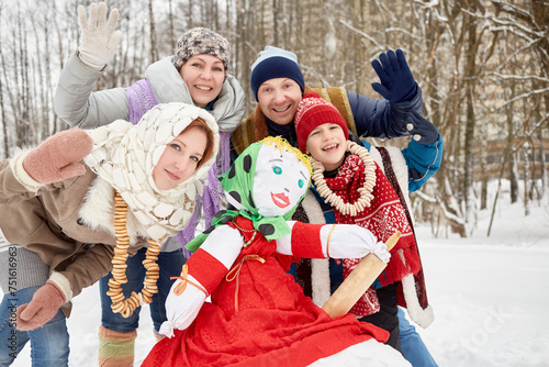 Happy family of four wave hands around stuffed dummy Maslenitsa in winter park