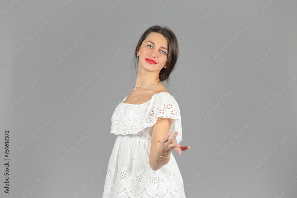 Half-length portrait of woman in white dress looking at us, stretches out her hand, on gray background Half-length portrait of woman in white dress looking at us, stretches out her hand, on gray background