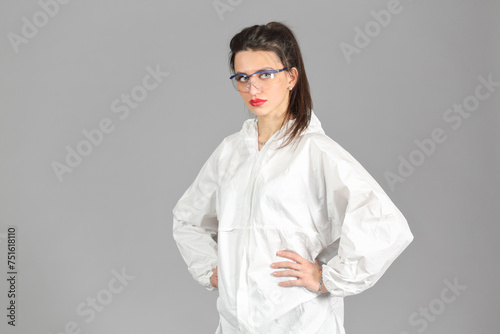 Half-growth portrait of woman in white protective suit of synthetic paper, looking at us, hands on waist, on gray background photo
