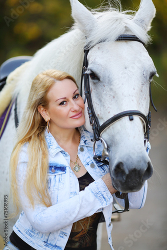 Woman with white hair poses with white horse in sunny autumn park