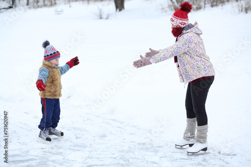 Mother and her cute little son learn to skating on ice in winter day