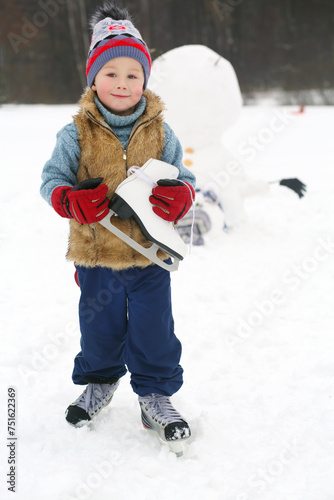 Little handsome boy with skate stands near upside down snowman at winter day photo