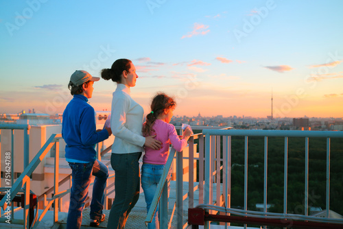 Fototapeta Naklejka Na Ścianę i Meble -  Mother with son and daughter standing on roof of multistory house and looking into distance