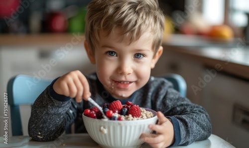 Small kid eating oatmeal with blueberries and raspberries from white bowl