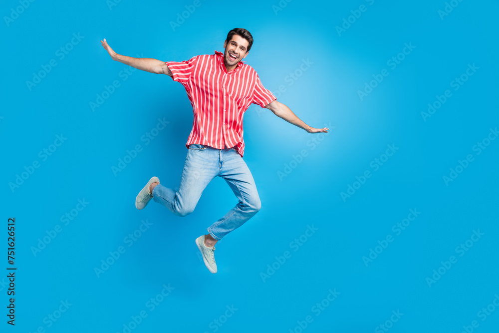 Full body photo of childish carefree guy wear stylish shirt jeans trousers flying hold palms like wings isolated on blue color background