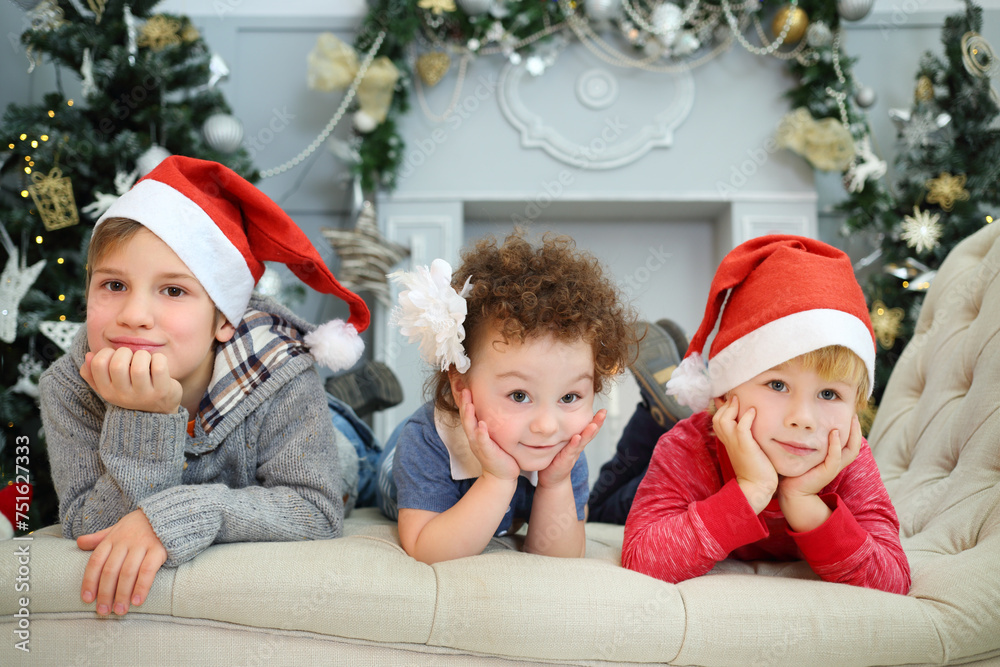 Three happy cute children in santa caps lie on couch and smile