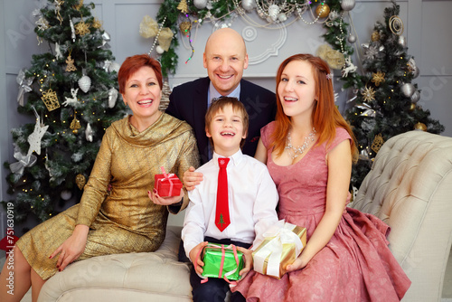 Mother, father, son and daughter sit on couch with gifts during christmas