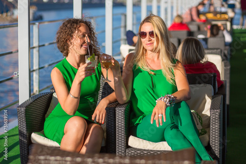 Two women in green with alcohol in ship restaurant during sailing on river