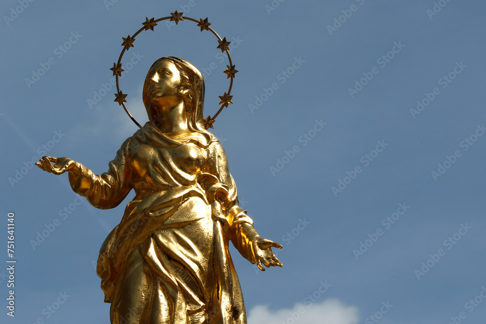 Golden Virgin Mary statue against blue sky.