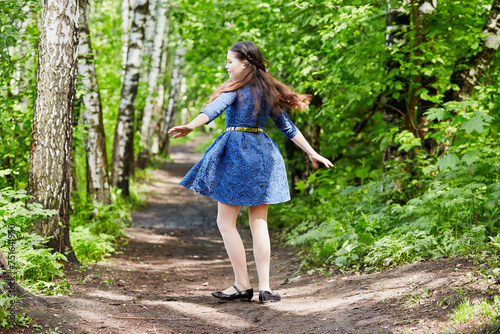 Little girl in dark-blue dress spins in dance on pathway in summer park