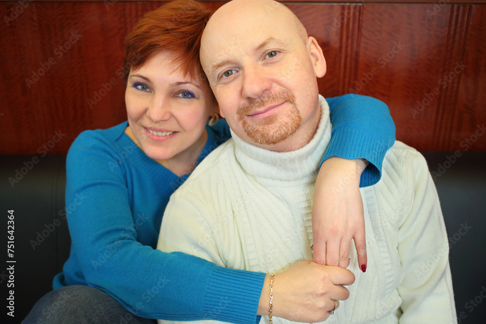 Portrait of a bald man and a red-haired woman sitting on a black sofa Portrait of a bald man and a red-haired woman sitting on a black sofa