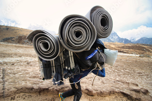 Fotografi Sherpa Porter carrying a heavy load on the Everest base camp trek trails towards