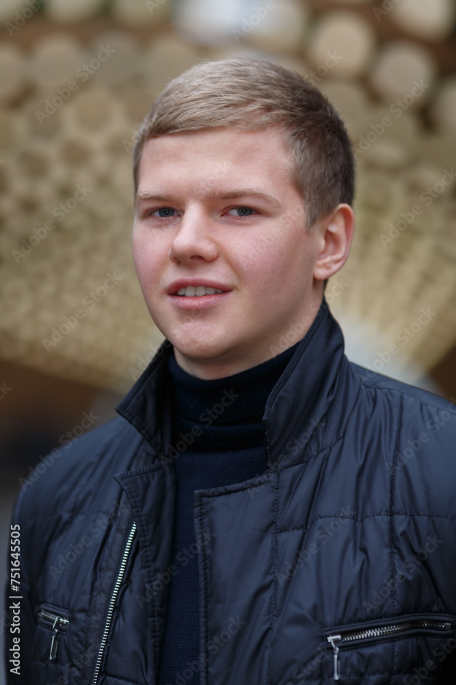Fototapeta premium Portrait of young blond man on background of lights installation main park alley, close-up