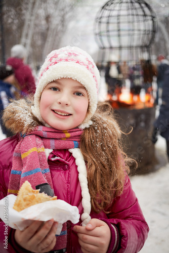 Smiling girl with meat pastry in hand in winter park with street fireplace photo