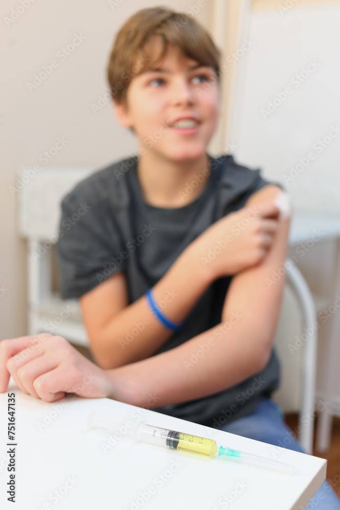 Young smiling boy rubbing tissue paper on his hand before injection, focus on the syringe lying on the table Young smiling boy rubbing tissue paper on his hand before injection, focus on the syringe lying on the table