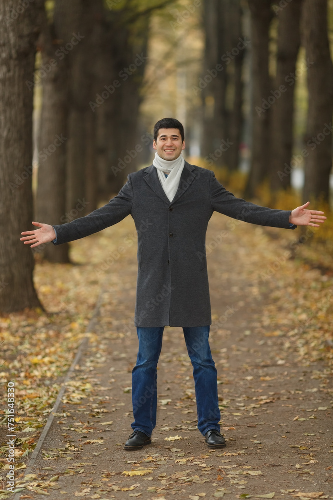 Portrait in full growth young man in gray coat with outstretched hands on alley in autumn park Portrait in full growth young man in gray coat with outstretched hands on alley in autumn park