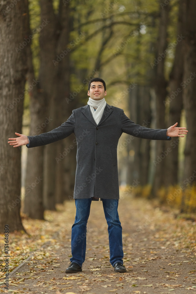 Portrait in full growth young man in gray coat with outstretched hands on alley in autumn park, looking up Portrait in full growth young man in gray coat with outstretched hands on alley in autumn park, looking up