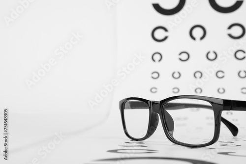 Vision test chart and glasses on white background, closeup. Space for text