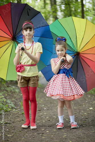 Two girls stands with rainbow coloured umbrellas in summer park photo